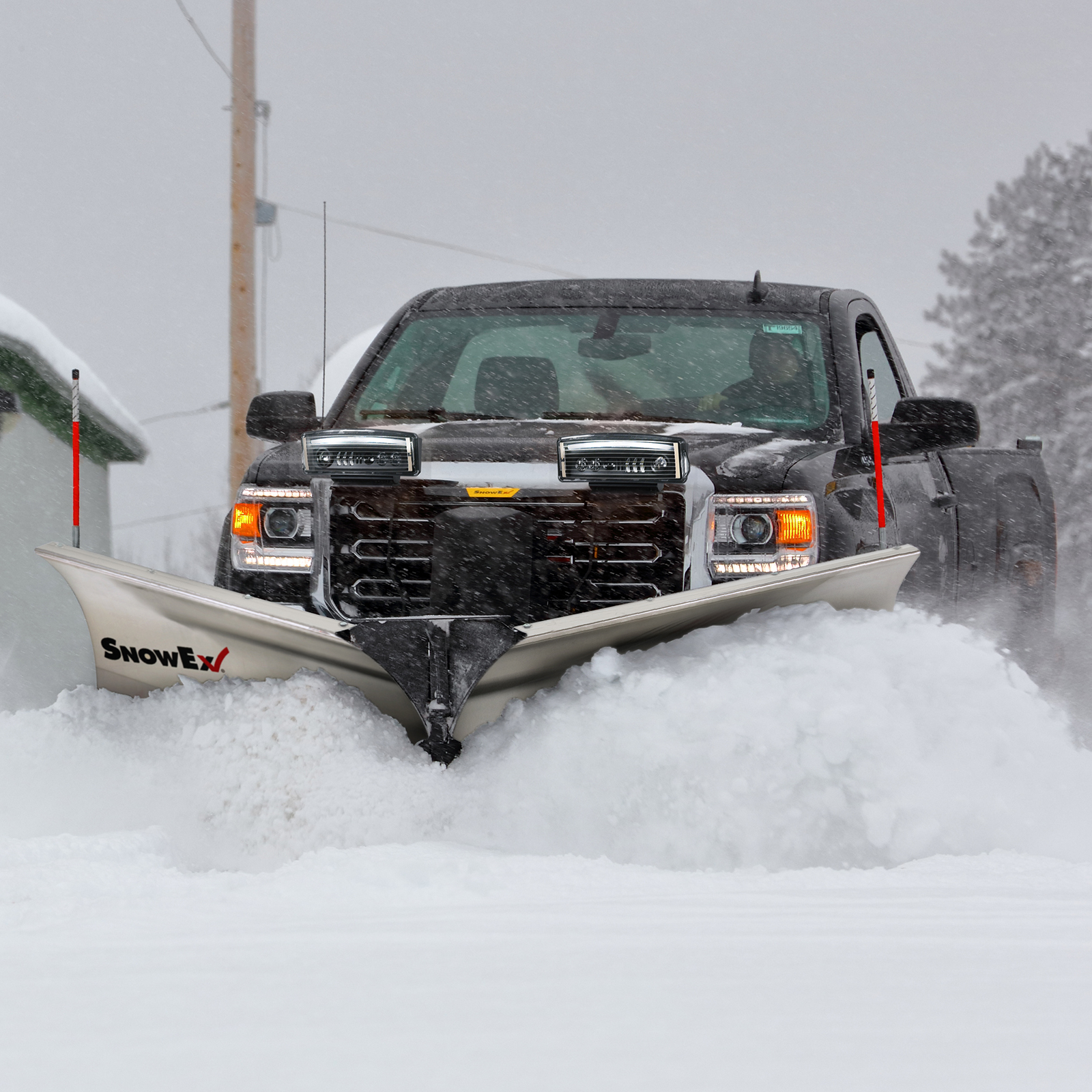 A black pickup truck with a large snowplow attachment clears deep snow from a road