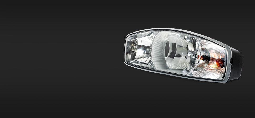 A close-up view of a vehicle headlight with a sleek, modern LED design, shown against a plain, dark background.