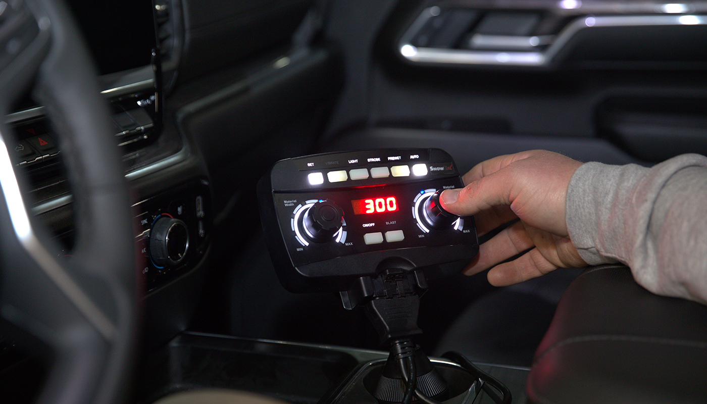 A person adjusts a control knob on an electronic device with a digital display reading 300, mounted inside a vehicle near the center console, ensuring precise operation.