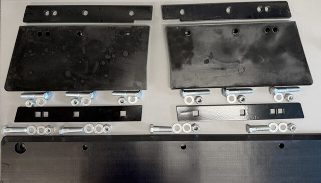 Several black metal or plastic plates of various shapes are laid out on a table, along with bolts, nuts, washers, and rectangular metal brackets arranged in organized rows.
